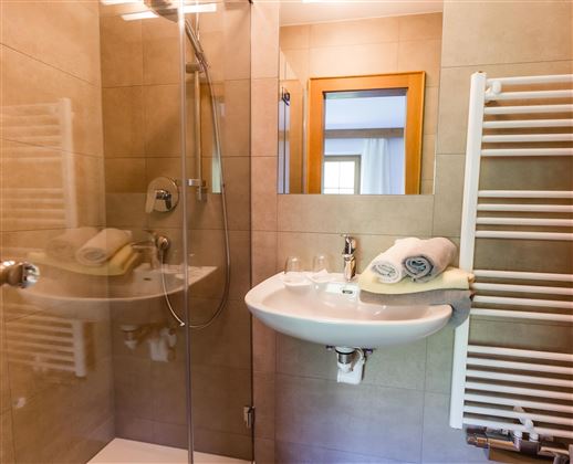 Ein modernes Badezimmer mit einer Dusche, einem Waschbecken und Handtüchern. Die Wände sind mit hellen Fliesen gefliest und es gibt einen Handtuchtrockner.