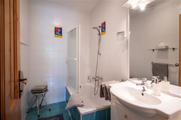 Ein modernes Badezimmer mit einer Badewanne und einer Dusche. Helle Fliesen und einige dekorative Bilder an der Wand sorgen für eine freundliche Atmosphäre.