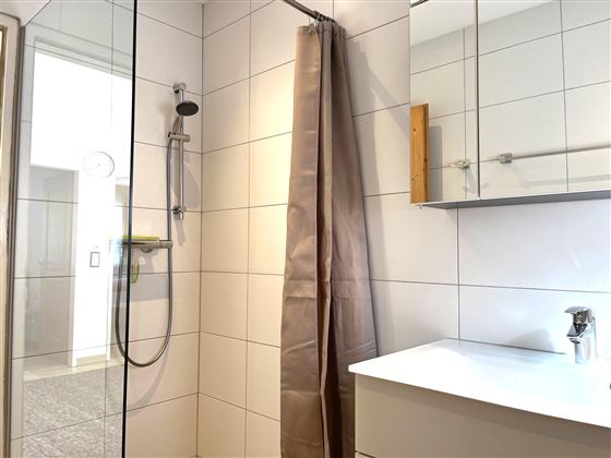 Ein modernes Badezimmer mit einer Dusche und einer großen Spiegelschranke. Die Wände sind hell gefliest und der Raum wirkt sauber und einladend.