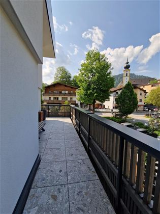 Ein Blick auf einen Balkon mit einem schönen Ausblick auf ein kleines Dorf. Im Hintergrund sind grüne Bäume und eine Kirchturm zu sehen.