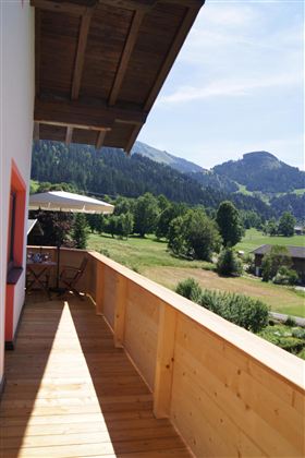 Ein schöner Balkon mit Holzgeländer und Blick auf grüne Wiesen und Berge. Die umliegende Landschaft ist sonnig und einladend.