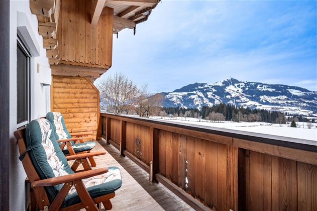 Ein charmantes Chalet im Winter mit Schnee auf dem Boden. Im Hintergrund sind verschneite Bäume und ein klarer blauer Himmel zu sehen.