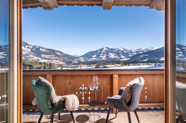 A beautiful balcony with two comfortable chairs and a view of the snow-covered mountains. The sky is clear and blue, perfect for relaxing.