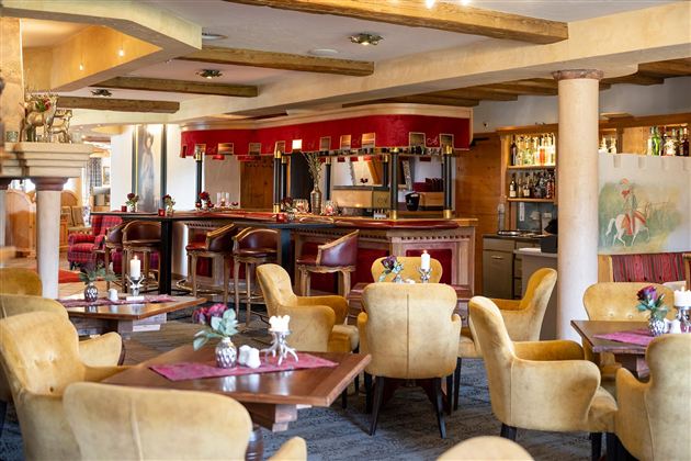 Ein elegantes Restaurant mit gemütlichen, gelben Sesseln und Holztischen. Die Bar im Hintergrund ist gut ausgestattet und lädt zum Verweilen ein.