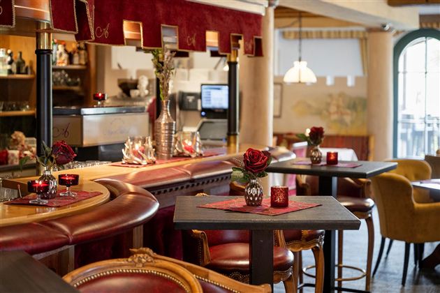 Eine gemütliche Bar mit stilvollem Interieur und roten Akzenten. Auf den Tisch stehen Kerzen und kleine Blumenarrangements.