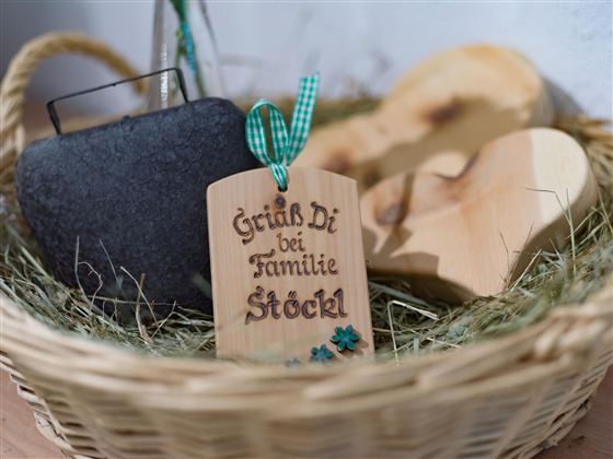 A decorative basket with a wooden sign that says "Grüß Di bei Familie Stöckl." The basket also contains a stone and two wooden hearts.