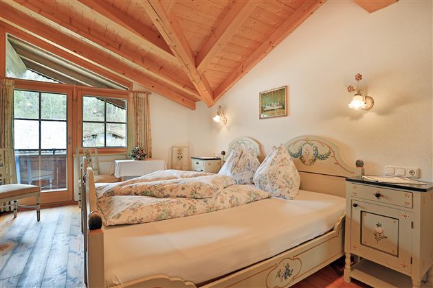 Een gezellige slaapkamer met schuine houten balken en een groot raam. De kamer is uitgerust met een tweepersoonsbed en stijlvolle meubels in traditionele stijl.