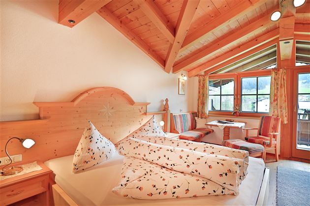 Een gezellige slaapkamer met houten decor en grote ramen. De kamer is licht en vriendelijk, met een kleine tafel en stoelen.