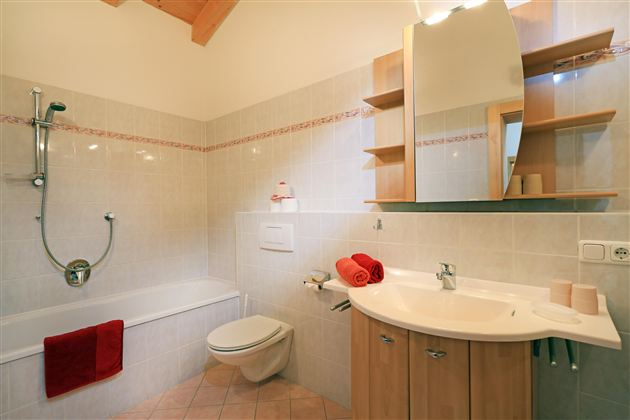 Een moderne badkamer met een bad en een douche. De ruimte is licht en biedt houten planken en handdoeken in warme tinten.