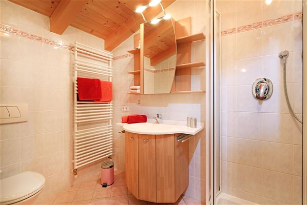 Een moderne badkamer met een houten kast en een grote spiegel. De muren zijn licht betegeld en er zijn handdoeken in stralend rood.