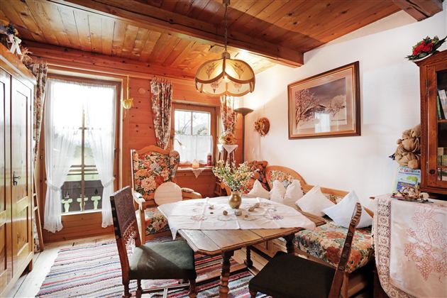 Een gezellige eetruimte met een ronde tafel en bloemige meubels. Grote ramen laten veel licht binnen en creëren een uitnodigende sfeer.