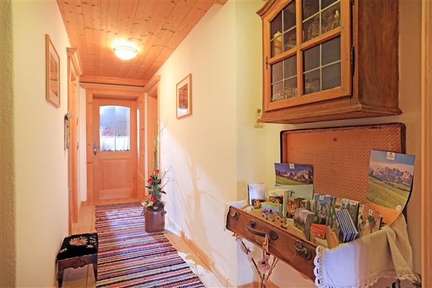 Een uitnodigende hal met houten plafond en kleurrijk tapijt. Een dressoir met ansichtkaarten en een plant geeft de ruimte een gezellige sfeer.