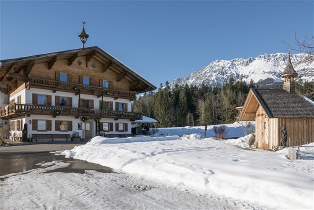 A traditional wooden house in the snow with a picturesque mountain in the background. The clear winter landscape conveys a calm and inviting atmosphere.