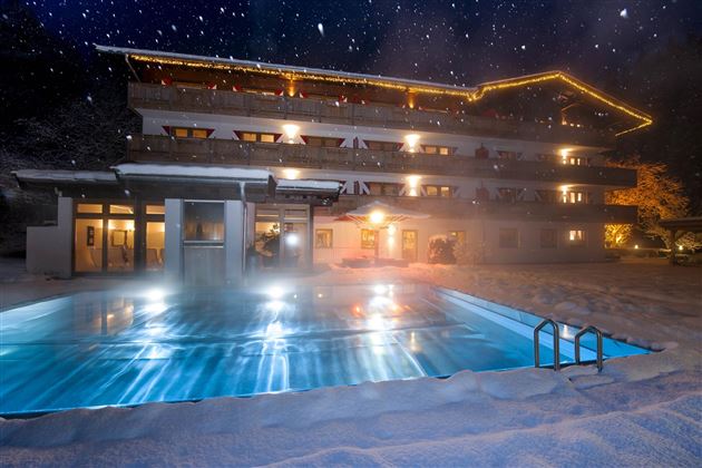 Ein gemütliches Hotelgebäude im Schnee mit einem beleuchteten Pool. Der Nachthimmel ist klar und sternenklar.