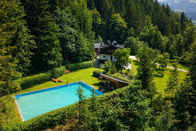 An idyllic house amidst trees with a blue swimming pool. The green space around the house invites you to relax and linger.