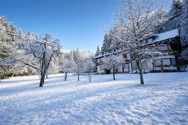 A snow-covered house in a winter landscape. The trees and the ground are covered with a thick layer of snow.
