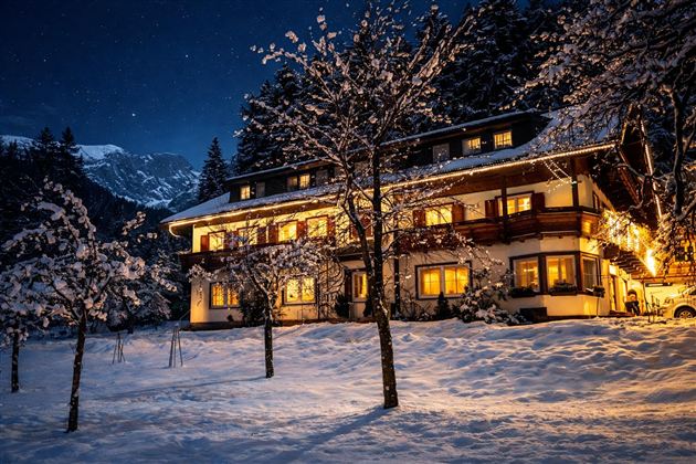 A cozy house in the snow, illuminated by warm light. The night sky is clear and dotted with stars.