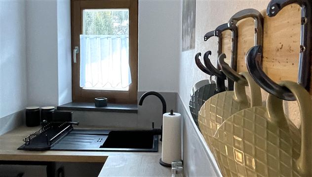 Een moderne keuken met een elegant wastafel en houten planken. Aan de muur hangen praktische keukengereedschappen.