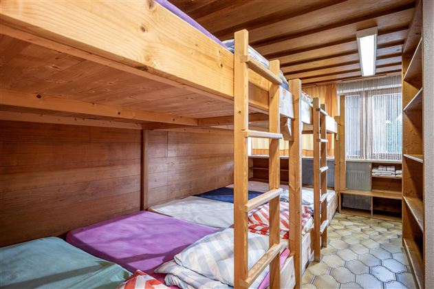 Ein Schlafsaal mit zwei Etagenbetten aus Holz. Das Zimmer hat einen hellen Holzlook und ein Fenster, das Tageslicht hereinlässt.