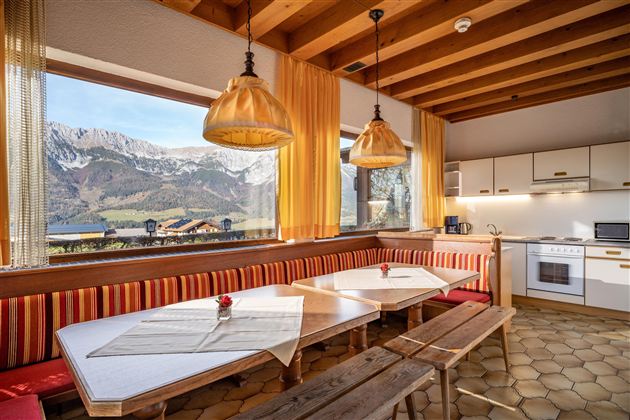 Ein gemütlicher Essbereich mit großem Tisch und Holzbänken. Durch die Fenster sieht man die schneebedeckten Berge und die wunderschöne Landschaft.