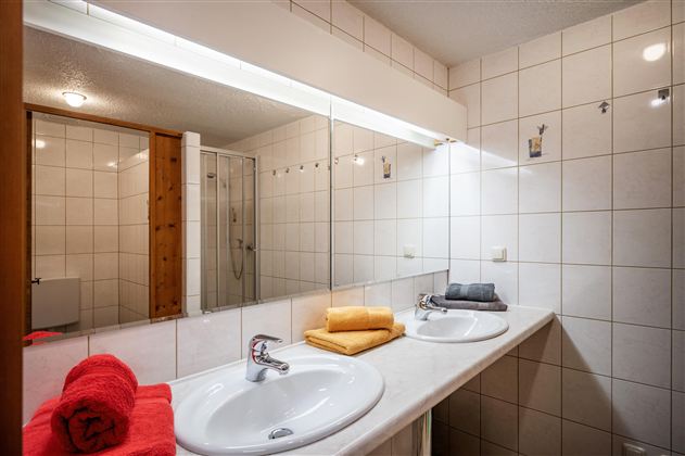 Ein helles Badezimmer mit zwei Waschbecken und großen Spiegeln. Bunte Handtücher in Rot und Gelb sind ordentlich platziert.