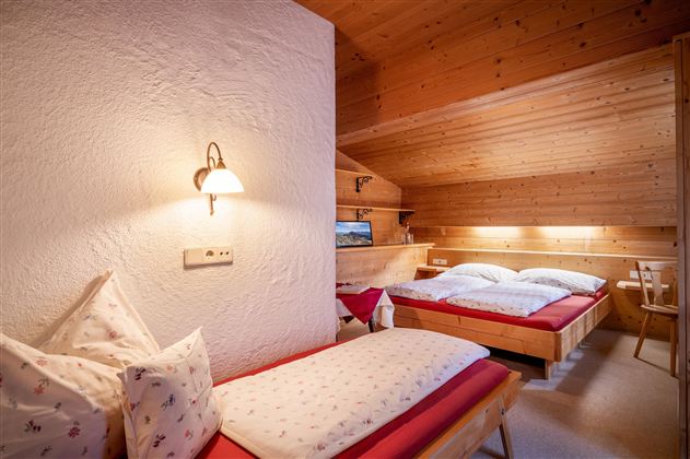 Ein gemütliches Schlafzimmer mit Holzverkleidung und zwei Betten. Die ruhige Atmosphäre wird durch warmes Licht und einfache Dekoration unterstrichen.