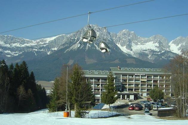 A picturesque mountain landscape with snow-covered peaks and a hotel in the foreground. A cable car floats above the scene.