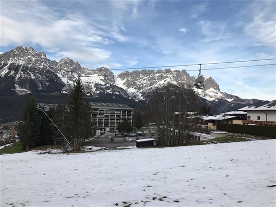 A snow-covered landscape with impressive mountains in the background. In the foreground, there is a building and a cable car.