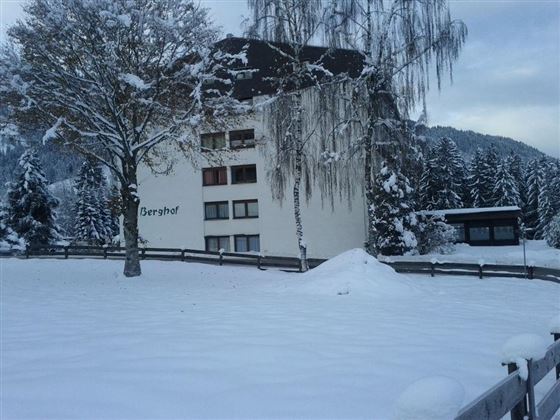A snow-covered building with the inscription "Berghof". In the background, snow-covered trees and hills are visible.