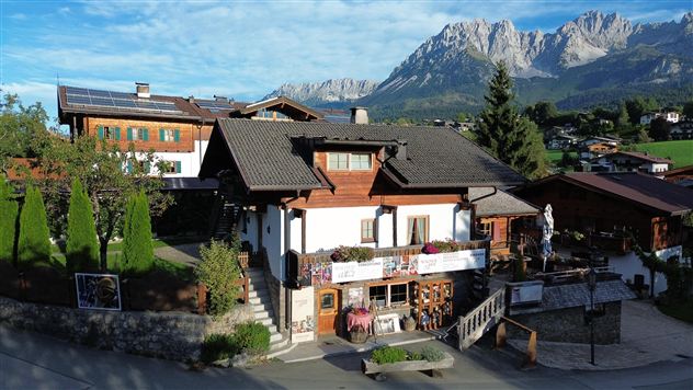 Ein malerisches Haus in den Alpen mit traditionellen Holzverkleidungen. Im Hintergrund sind majestätische Berge und ein klarer Himmel zu sehen.