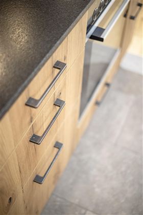 A modern kitchenette with wooden fronts and a black countertop. The furniture is designed to be simple and functional.