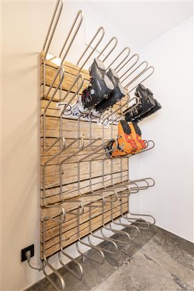 A stylish frame made of wood and metal for storing ski boots. Several compartments are visible, in which some boots are placed.