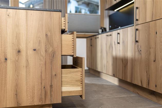 A modern kitchen with wooden cabinets and open drawers. The floor is tiled with gray tiles.