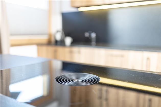 A modern kitchen with a black countertop. In the foreground, a round drain is visible.