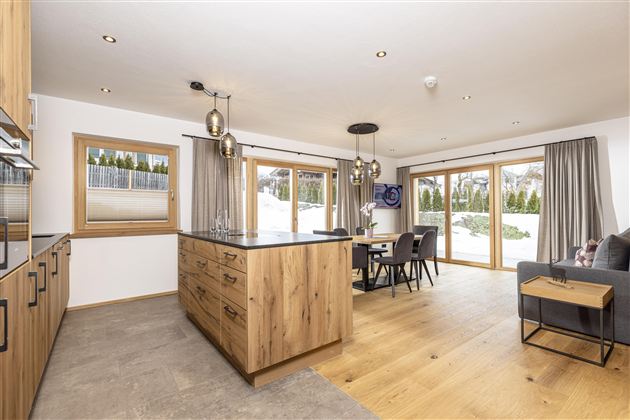 A modern kitchen with a wood island and plenty of natural light. The space is bright and inviting, with a dining table and a cozy living area.