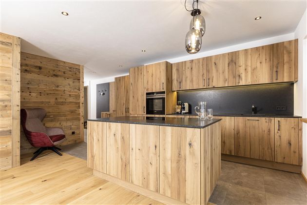 Eine moderne Küche mit Holzmöbeln und einer großzügigen Kochinsel. Sie bietet stilvolle Beleuchtung und hat ein warmes, einladendes Ambiente.