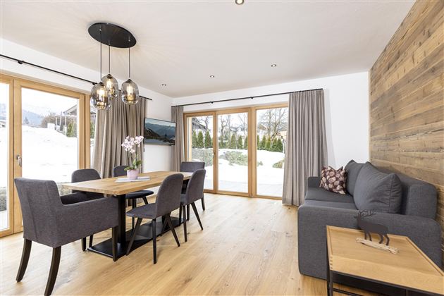 A modern dining room with a wooden table and comfortable chairs. Large windows offer a view of the snowy landscape.