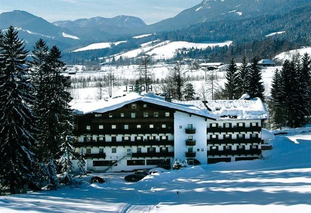 Een elegant hotel in de sneeuw met een pittoresk bergpanorama op de achtergrond. Omringd door hoge, besneeuwde dennenbomen strekt het winterse landschap zich uit.