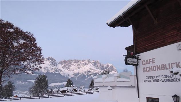 Snow-covered mountains in the background and a charming café in the foreground. The landscape is peaceful and wintry.
