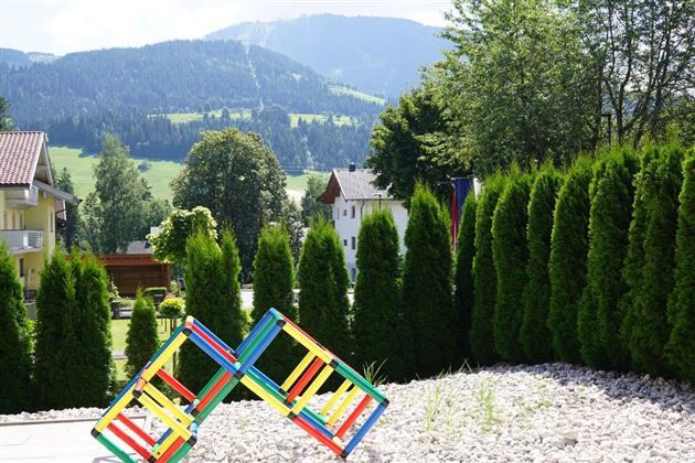 Een kleurrijke speeltuin met een unieke houten structuur. Op de achtergrond strekken groene heuvels en bomen zich uit onder een blauwe lucht.