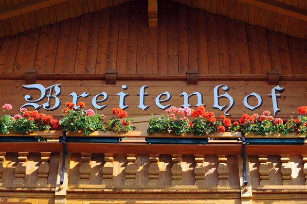 A wooden building with the inscription "Breitenhof" and colorful flower boxes. The façade radiates a cozy atmosphere.