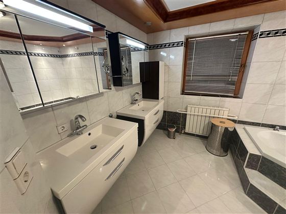 Ein modernes Badezimmer mit weißen Waschbecken und großen Spiegeln. Die Wände und der Boden sind mit hellen Fliesen ausgestattet, und es gibt eine Badewanne sowie eine Heizung.