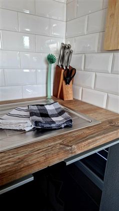 Een moderne keukentafel van hout met een gootsteen. Er liggen vaatdoeken en keukenhulpmiddelen op de tafel.