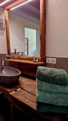 Een moderne badkamer met een houten wastafel en een rond wasbak. Op de tafel liggen zachte handdoeken en in de spiegel weerspiegelt zich een gezellige sfeer.