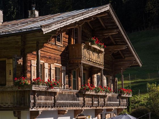Ein traditionelles Holzhaus mit blühenden Balkonkästen. Es befindet sich in einer malerischen, grünen Landschaft.