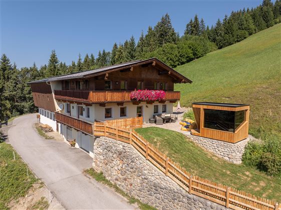 Ein idyllisches Haus in den Bergen mit Holzbalkons und bunten Blumen. Umgeben von grünen Wiesen und Bäumen ist es ein perfekter Rückzugsort in der Natur.