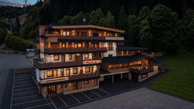 Ein modernes Gebäude mit mehreren Stockwerken, das gemütliche Apartments bietet. Die Fassade ist aus Holz und Stein, umgeben von grünen Bäumen.