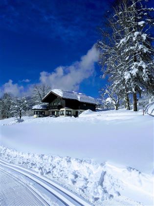 A beautiful, snow-covered house in a winter landscape. The sky is clear and blue, surrounded by snow-covered trees.