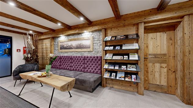 A cozy reception area with a purple sofa and a wooden table. A bookcase with informational materials stands against the wall.