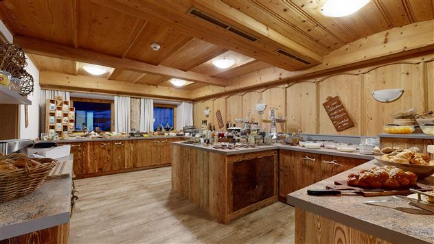 A cozy kitchen with wooden walls and an inviting atmosphere. Various foods and baked goods are arranged on the tables.